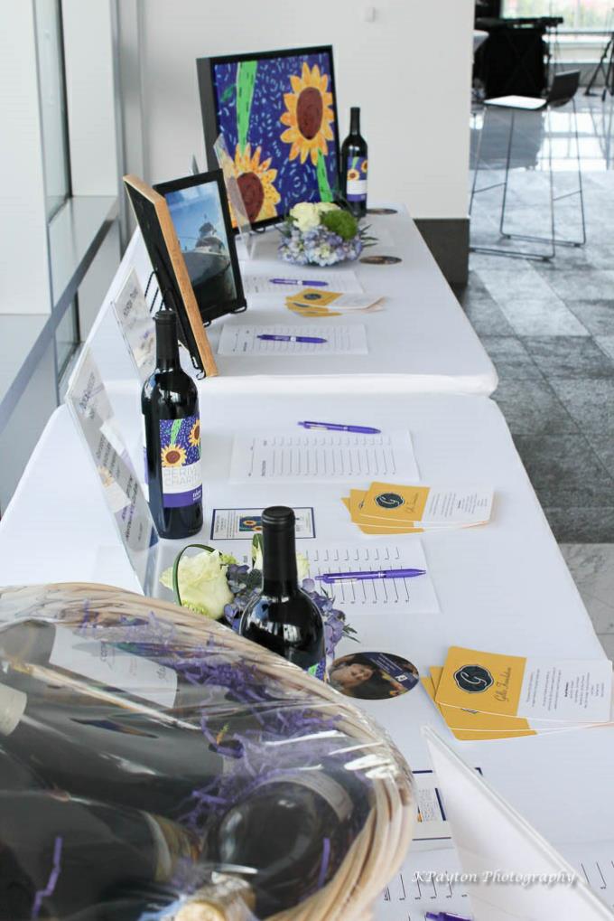 silent auction table display showing bottles of wine and a painting of sunflowers
